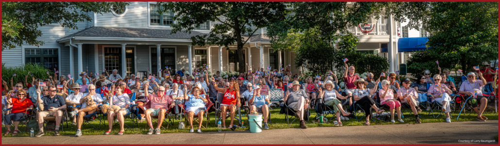 Large crowd seated on lawn chairs waving flags during Patriotic Pops 2025 event in front of Oakwood Resort.